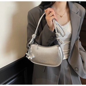 Detail of silver metallic crescent bag with knotted shoulder strap and chrome ball charm