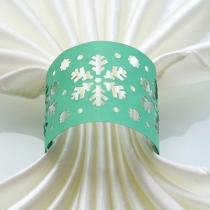 Macro detail of laser-cut mint green snowflake paper napkin ring on a white satin napkin