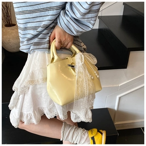 Detail of yellow patent leather tote with pearl pendant and lace bow accessory