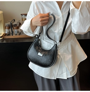 Detail of black woven crescent bag with metal logo plate and smooth leather texture