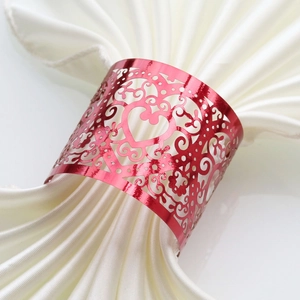 Detailed laser-cut scrollwork on red heart napkin ring over white satin fabric