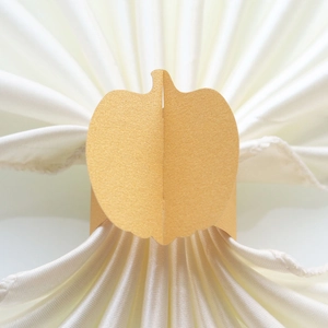 Macro shot of a golden pumpkin-shaped paper napkin ring on a satin white fabric napkin