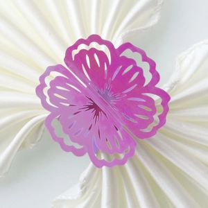 Close-up of laser-cut purple flower paper napkin ring on white satin fabric