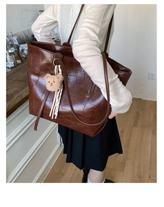 Detail of deep brown crocodile embossed faux leather tote bag with plush bear charm accessory