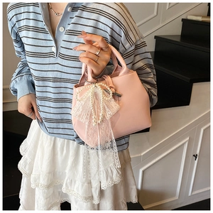 Detail of pink faux leather handbag featuring pearl handle rings and a lace bow charm
