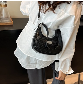 Detail of black woven hobo bag with silver logo plate on a model wearing white shirt