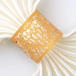 Detailed view of golden laser-cut heart napkin ring on a white satin cloth