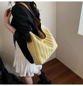 Close-up of a striped yellow and white canvas tote bag with brown leather shoulder straps