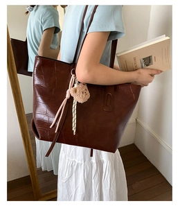 Detail view of brown crocodile pattern tote bag with teddy bear charm on model shoulder