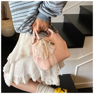 Detail of pink glossy leather handbag featuring pearl strap and white lace bow charm