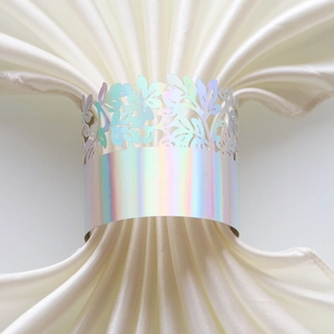 Detailed macro view of laser-cut holographic leaf napkin ring on white satin fabric