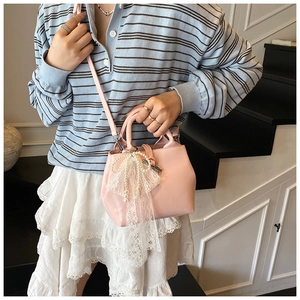 Detail view of pink bucket bag with lace bow and pearl pendant on a stylish model