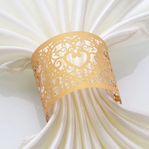 Close-up of golden laser-cut heart napkin ring with baroque patterns on white silk