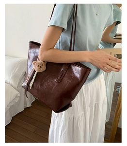 Brown crocodile embossed tote bag with plush bear charm worn on shoulder