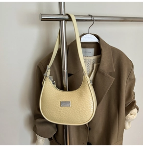 Detail of pale yellow hobo bag with woven texture and silver metal plate on a hanger