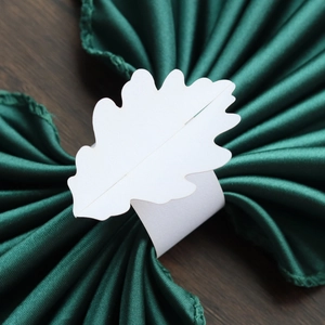 Gros plan du rond de serviette en papier blanc en forme de feuille sur tissu satiné vert