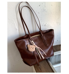 Close-up of dark brown crocodile embossed tote bag with plush bear charm and pink tassel