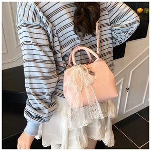 Detailed side view of pink patent leather handbag with lace bow and pearl charm