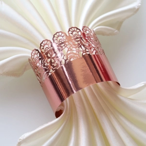 Close-up of rose gold hollow crown napkin ring on a white satin cloth for wedding party