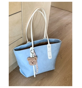 Detail of light blue faux crocodile tote bag with white straps and small bear charm