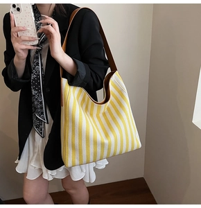 Detail of large striped tote bag with brown leather shoulder strap on a female model