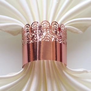 Detail of rose gold napkin ring with laser-cut lace crown design on satin fabric