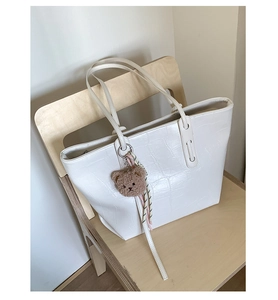 Detailed macro view of white crocodile pattern tote bag with brown plush bear accessory