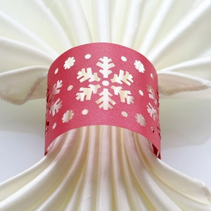 Detailed laser-cut red snowflake paper napkin ring on a beige silk cloth for Christmas