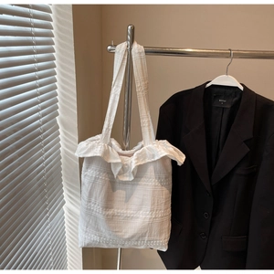 Détail d'un sac cabas blanc à volants suspendu à un cintre avec un blazer noir