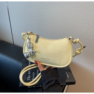 Detail of pale yellow crescent bag featuring wrinkled texture and silver balloon dog charm