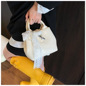 Detail of cream leather handbag with white lace bow and pearl chain charm