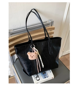 Detail of black crocodile embossed tote bag with teddy bear charm and woven tassel accent