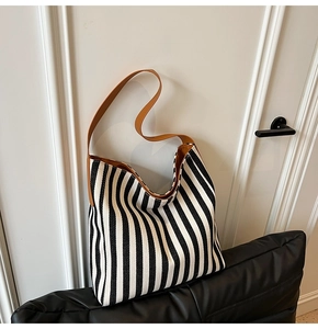 Detail of black and white striped canvas tote bag with brown leather handles on a leather cushion