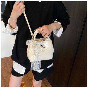 Detailed shot of cream white leather bucket bag featuring lace bow and pearl handle charm
