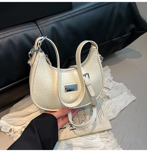 Close-up of beige crescent bag with crocodile embossed texture and silver hardware