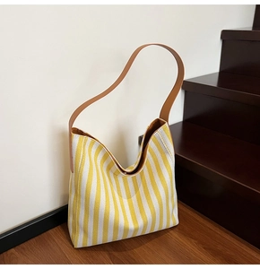 Detail of yellow and white striped canvas tote bag with brown leather shoulder straps