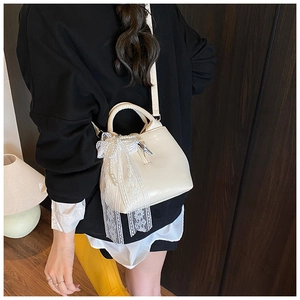Detail of a beige handbag with a large lace bow and elegant pearl chain accessory