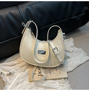 Detail of cream crescent bag with woven texture, silver logo, and adjustable straps