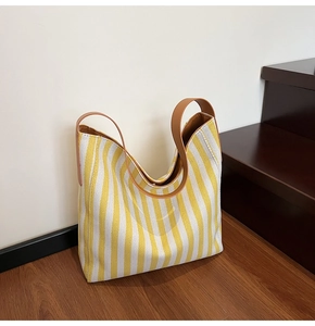 Detail of yellow and white striped canvas tote bag with brown leather handles on a staircase