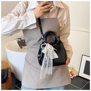 Glossy black patent leather handbag featuring lace and pearl bow charms on a model