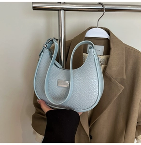 Detail of light blue crescent bag featuring woven texture and silver metal plaque