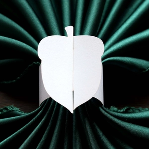 Macro view of white paper napkin rings with leaf design on dark green silk fabric