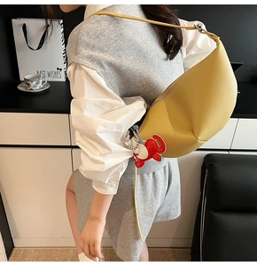 Detailed view of yellow lychee leather crescent bag with red elephant charm and wide strap