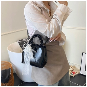 Close-up of black glossy bucket bag featuring white lace bow and pearl charm detail