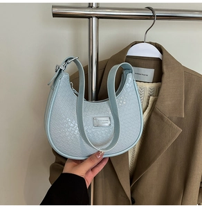 Detailed view of light blue crescent bag with woven texture and metal logo plaque