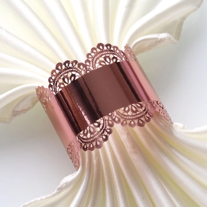 Detailed close-up of rose gold lace napkin ring with laser-cut floral pattern on silk