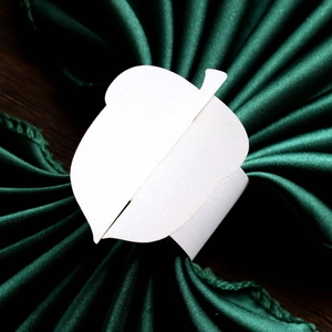 Macro shot of pearl white acorn shaped paper napkin ring on green silk fabric
