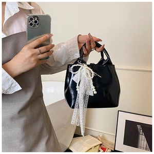 Close-up of black patent leather handbag with lace bow and pearl decoration