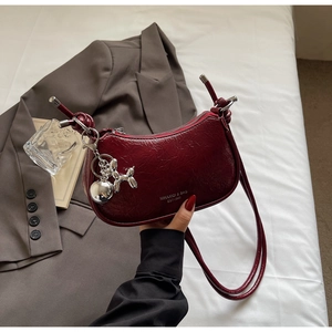 Close-up of wine red crescent shoulder bag with silver balloon dog charm and pleated texture