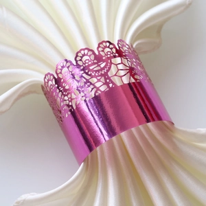 Detail of pink laser-cut lace napkin ring with mirror finish on white satin cloth